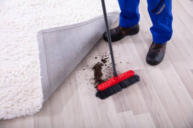 Lowsection View Of A Janitor Cleaning Dirt Under The Carpet With Mop