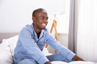 Yatakta oturan gülümseyen Afrikalı genç adam.