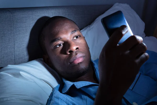 Africano Homem Deitado Cama Usando Telefone Celular Noite — Fotografia de Stock