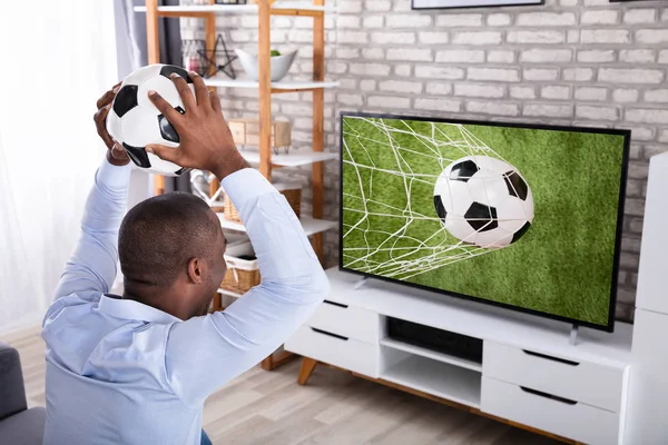 Afrykański Młody Człowiek Rzucanie Piłki Nożnej Telewizji Domu — Zdjęcie stockowe