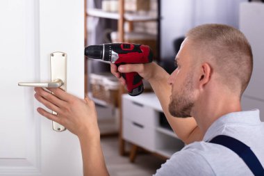 Male Carpenter Installing Door Lock With Wireless Screwdriver clipart