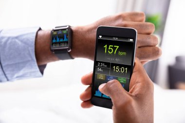 Bir adamın elini Smartwatch ve kalp atışı oranı gösterilen cep telefonu ile yakın çekim