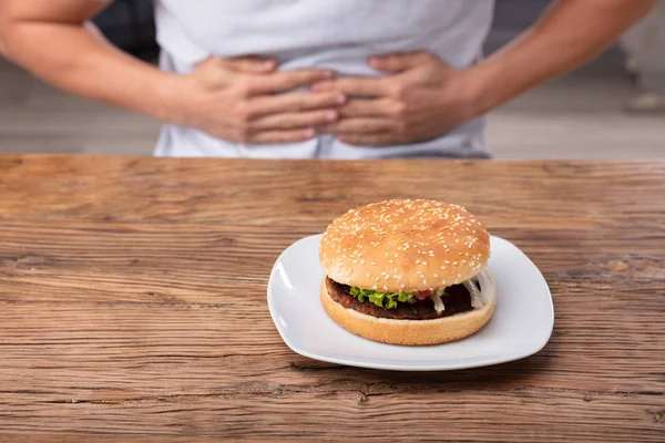 Man Having Stomach Pain Fresh Burger Plate Wooden Desk — Stock Photo, Image