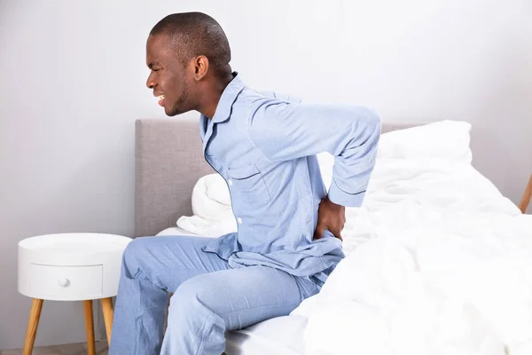Junger Mann Sitzt Auf Bett Und Leidet Unter Rückenschmerzen — Stockfoto