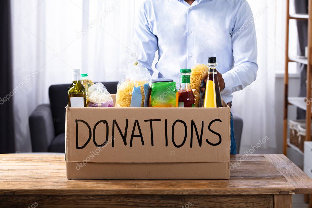 Man Standing With Various Food Items In Donation Box