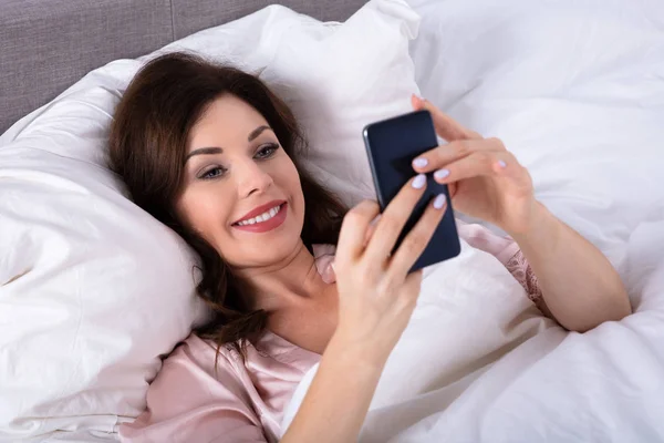 快乐的年轻女子躺在床上使用手机 — 图库照片