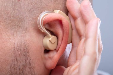 Kulağına işitme cihazı taktıktan sonra duymaya çalışan bir adamın elinin yakın çekimi.