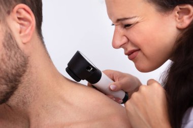 Dermatoskopla erkeğin boynundaki deriyi kontrol eden genç bir kadın doktorun yakın çekimi.