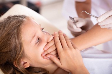 Diş tedavi kliniği giderken ağzını elleriyle kapsayan korkmuş bir kız