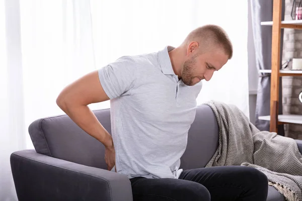 Hombre Joven Sentado Sofá Que Sufre Dolor Espalda —  Fotos de Stock