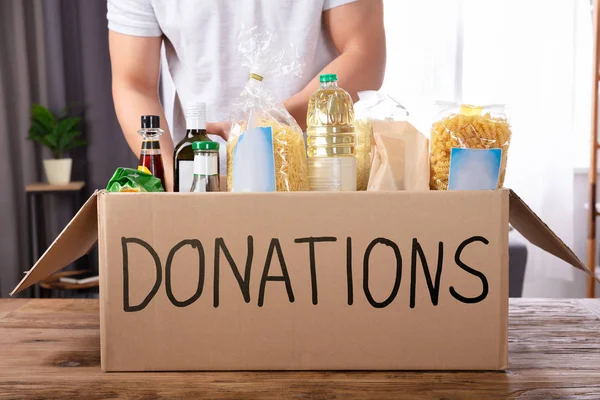 Young Man Putting Groceries Donation Box Wooden Desk — Stock Photo, Image