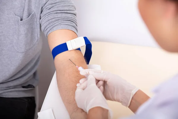 血液サンプルを収集するために患者の腕に注射器を注入する医師のクローズ アップ — ストック写真