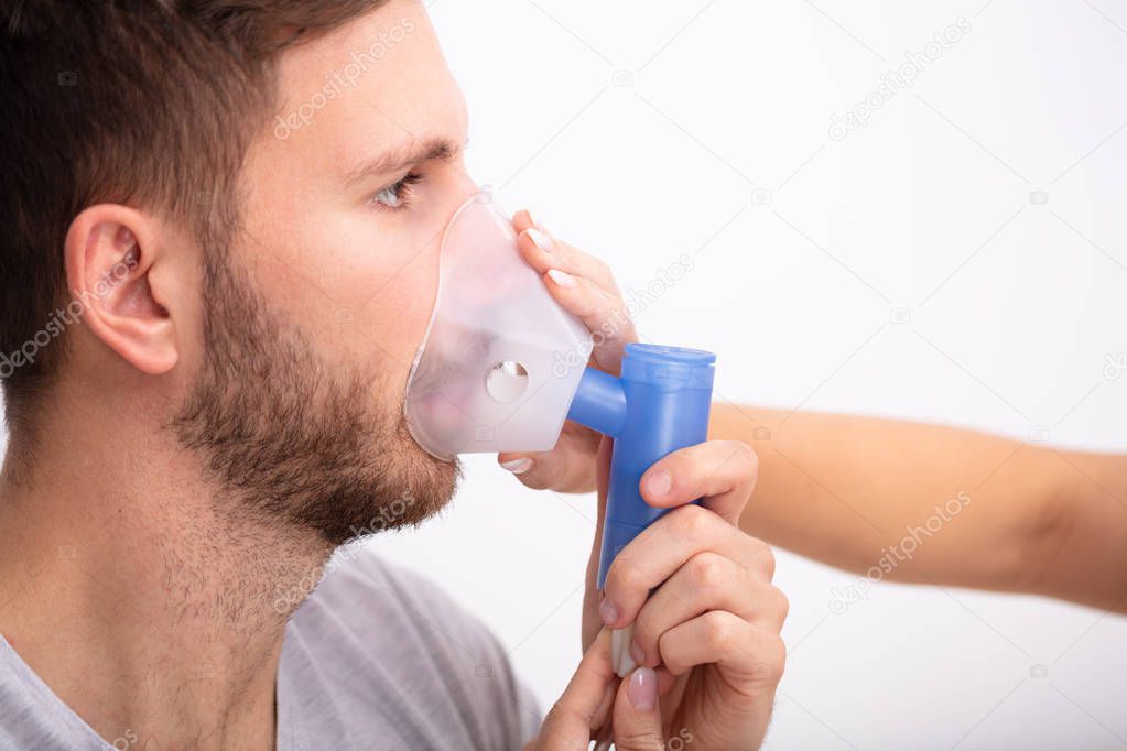 Side View Of Young Female Doctor Holding Oxygen Mask Over Male Patient's Mouth