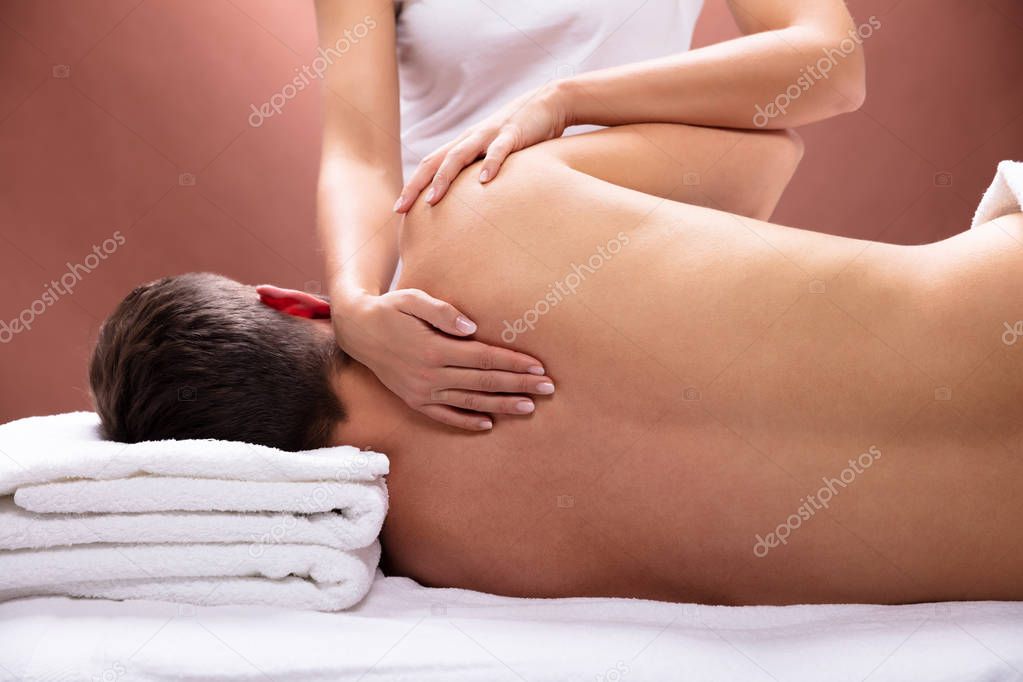 Close-up Of Therapist Hand Giving Shoulder Massage To Young Man