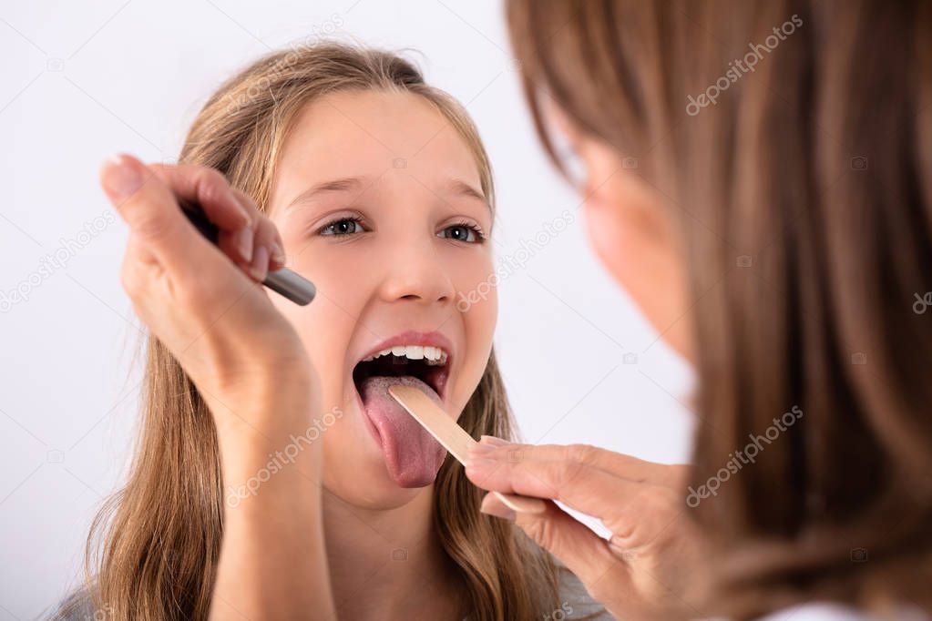 Close-up Of Doctor Checking Girl's Sore Throat With Tongue Depressor