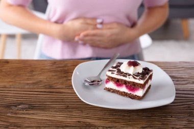 Karın ağrısı çeken bir kadının önündeki tabakta taze kekin dilimi.