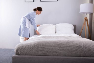 Gülümseyen kadın kahya otel odasında yatak yapma