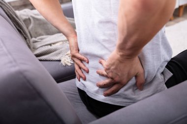 Close-up Of A Man Sitting On Sofa Having Back Pain clipart