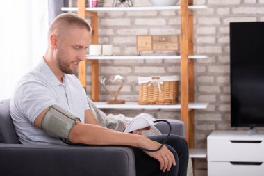 Koltukta oturan genç adam evde kan basıncını ölçüyor.