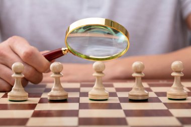 Büyüteç Camı piyon satranç parça üzerinde tutan bir erkek eli Close-up