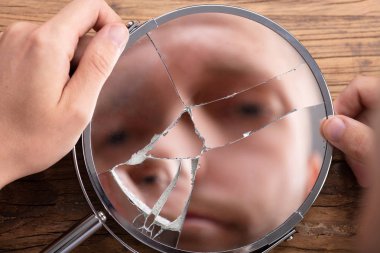 Close-up Of A Man's Face In Broken Mirror Over Wooden Desk clipart
