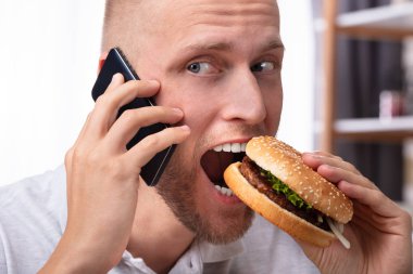 Cep telefonu incelerken Burger yemek genç bir adam portresi