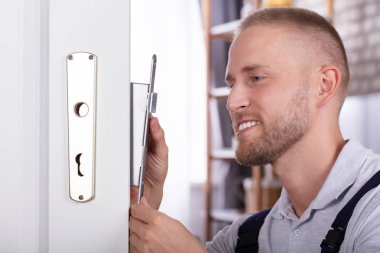 Close-up Of A Smiling Young Man Fixing Door Lock In House clipart