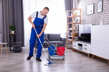 Gülümseyen erkek hademe oturma odasında paspasla yerleri temizliyor.