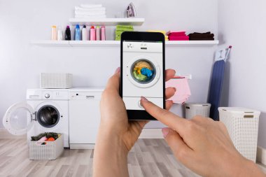 Çamaşır makinesi cep telefonu ile çalışan bir kadın eli Close-Up