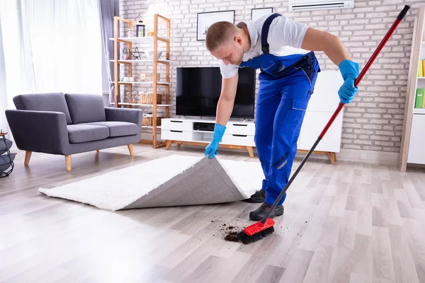Young Male Janitor In Uniform Removing Dirt Under The Carpet — Stock Image Young Male Janitor Uniform Removing Dirt Carpet Royalty Free Stock Images