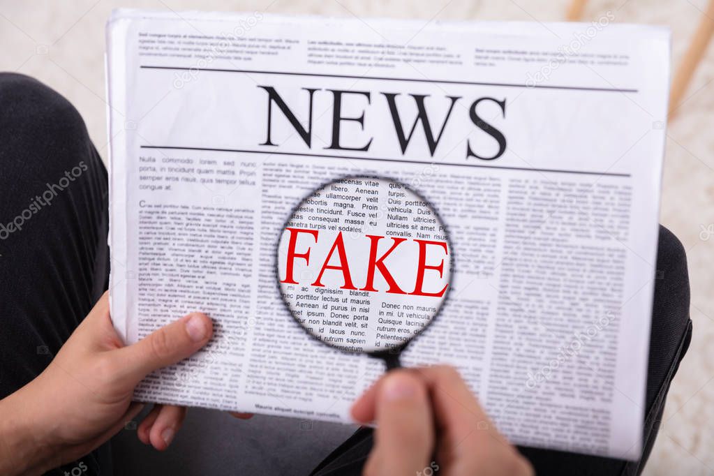 Man Examining Fake News On Newspaper Through Magnifying Glass