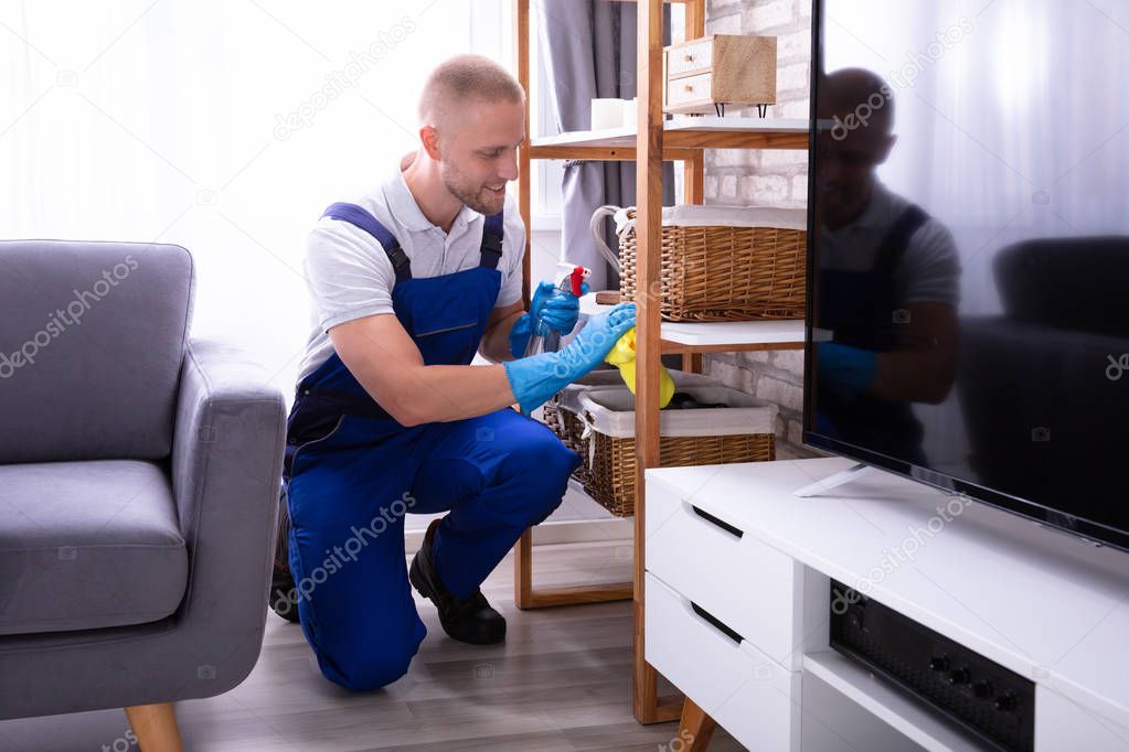 Smiling Male Janitor In Uniform Wiping Wooden Shelf