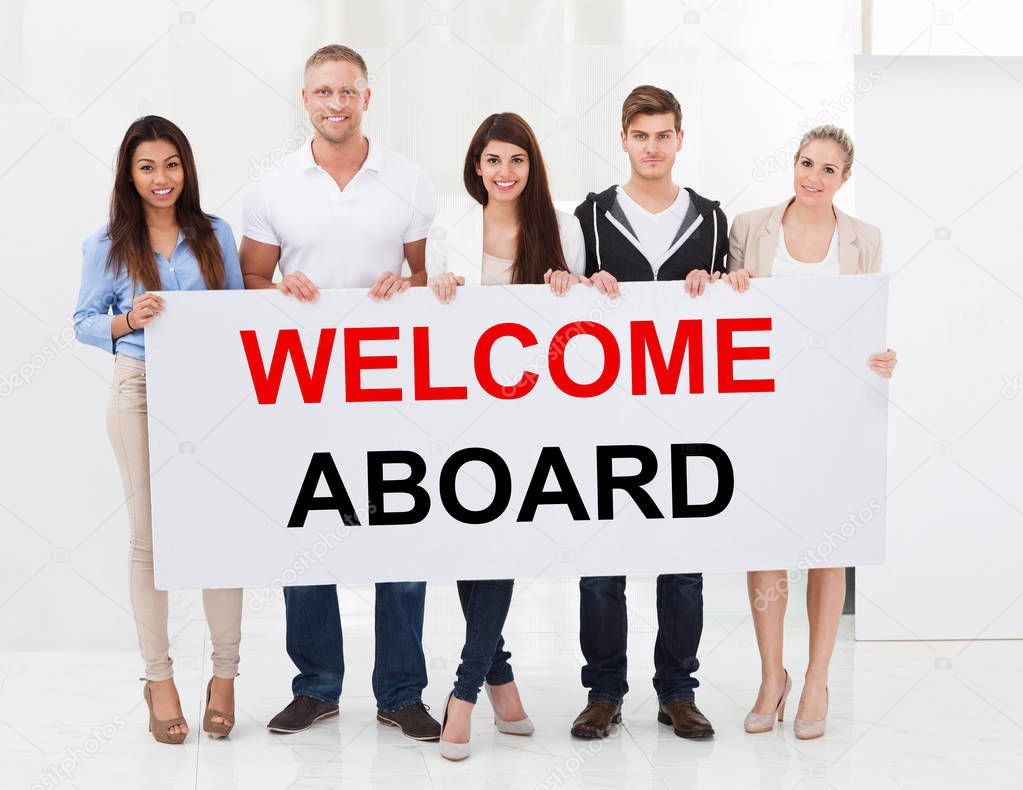 Group Of Happy People Standing Together With Welcome Aboard Placard