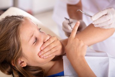 Diş tedavi kliniği giderken ağzını elleriyle kapsayan korkmuş bir kız