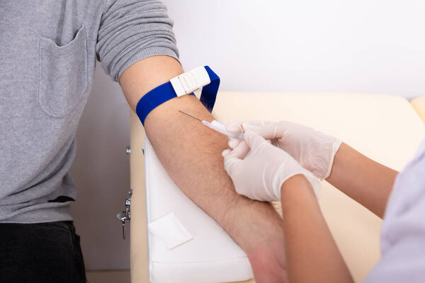 Young Female Doctor Injecting Male Patient With Syringe To Collect Blood Sample In Clinic