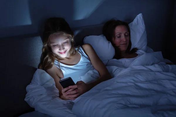 Chica Feliz Usando Teléfono Móvil Mientras Hija Duerme Una Cama — Foto de Stock