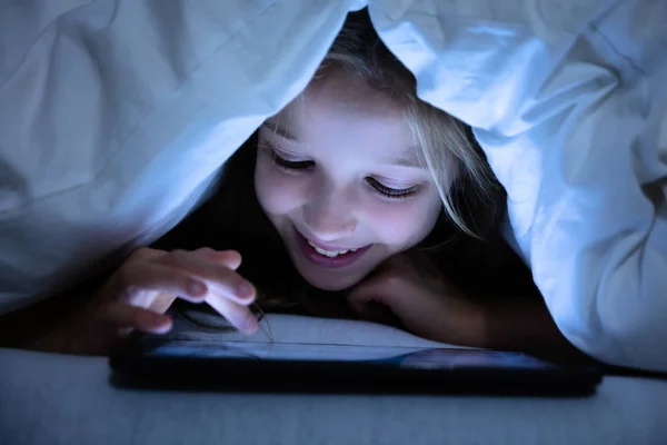 デジタルタブレットを使用して白い毛布の下で幸せな女の子のクローズアップ — ストック写真