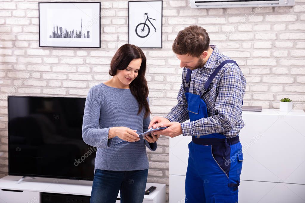 Male Technician Assisting Young Woman In Signing Invoice At Home