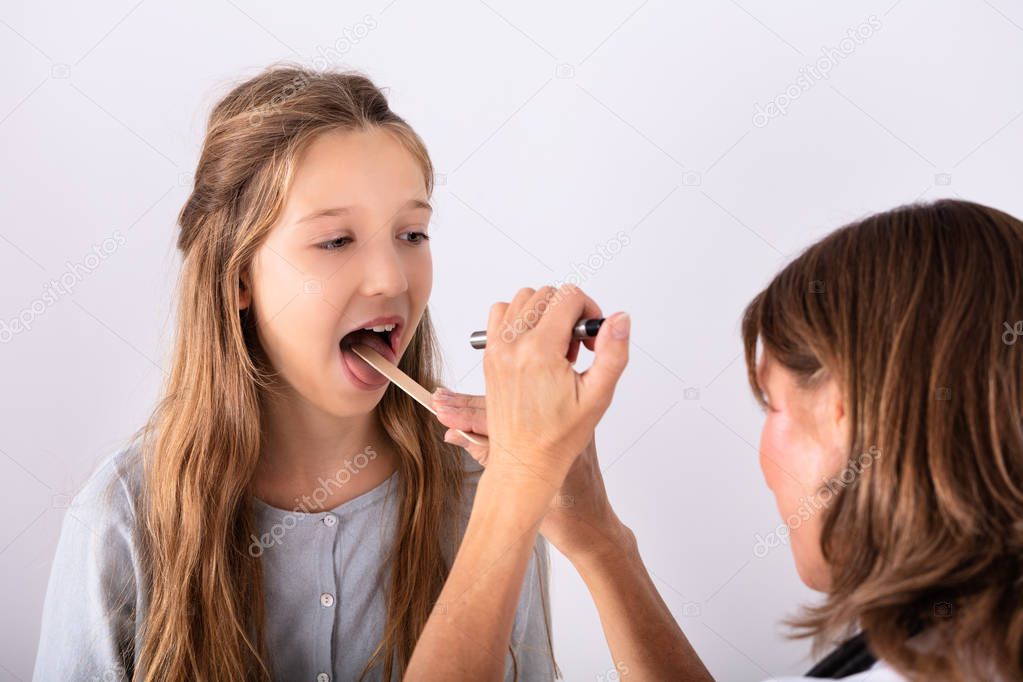 Close-up Of Doctor Checking Girl's Sore Throat With Tongue Depressor