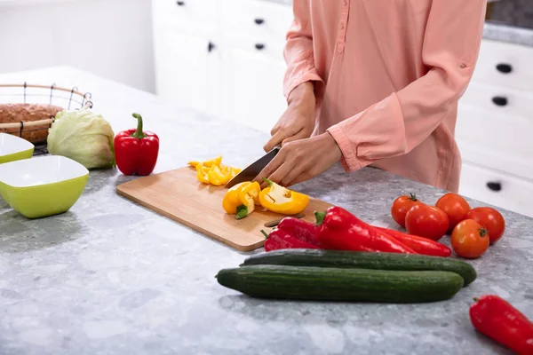 妇女切碎甜椒在切碎板上与刀在厨房柜台 — 图库照片