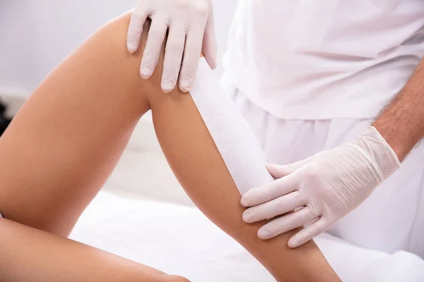 Male Beautician Hand Waxing Woman\'s Leg With Wax Strip