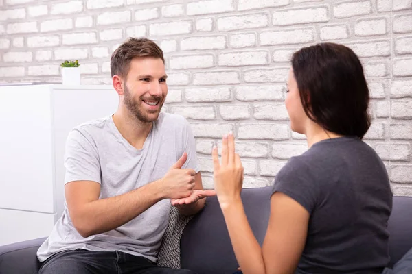 Sorrindo Jovem Casal Sentado Sofá Comunicando Com Língua Sinais — Fotografia de Stock