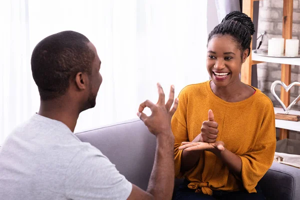 Sorrindo Jovem Casal Sentado Sofá Comunicando Com Línguas Gestuais — Fotografia de Stock