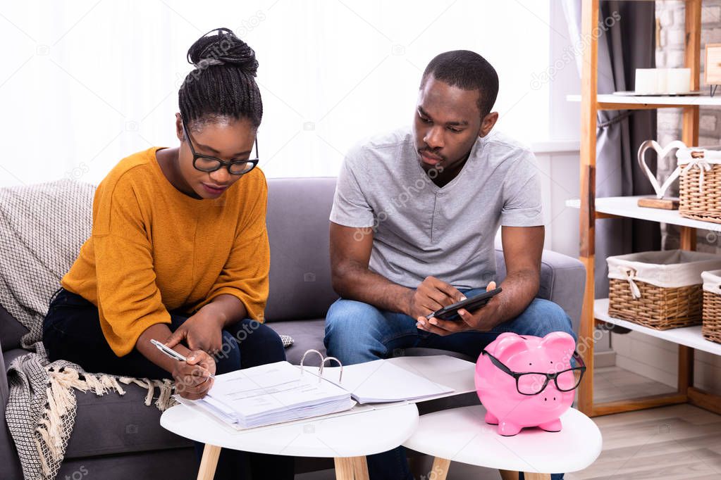 Young African Couple Sitting On Sofa Calculating Invoice