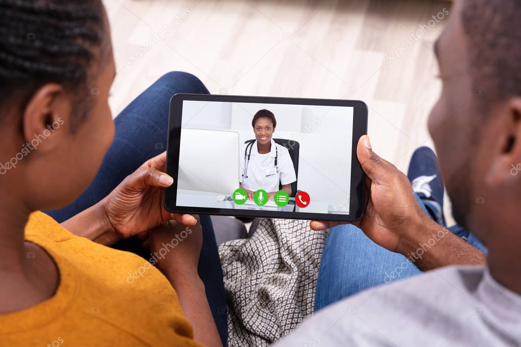 Close-up Of An African Couple Video Conferencing With Happy Female Doctor On Digital Tablet