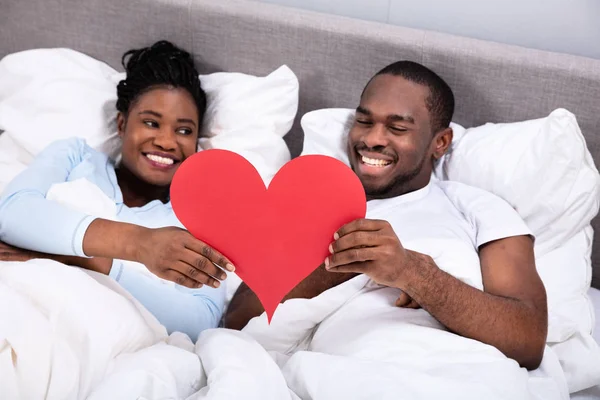 Sorrindo Jovem Casal Africano Deitado Cama Segurando Coração Vermelho — Fotografia de Stock