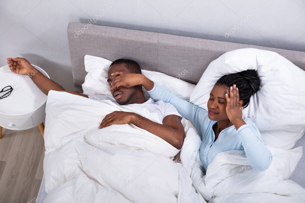 Disturbed Young African Woman Holding Her Husband's Nose To Stop Him From Snoring On Bed