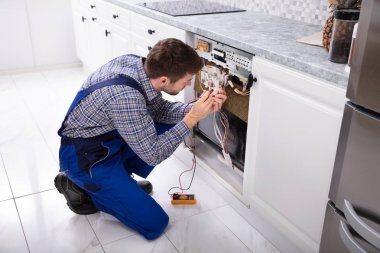 Genç tamirci mutfakta bulaşık makinesi dijital multimetre ile sabitleme
