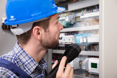 Close-up Of A Electrician Examining A Fuse Box With A Torch clipart