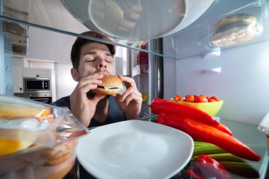 Aç bir genç adam Burger buzdolabı yeme Close-up